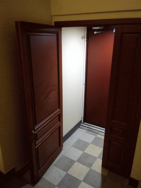 Показана деревянная вторая входная двустворчатая дверь в подъезде, парадной старого дома. Выполнена из массива сосны и покрашена в коричневый цвет.