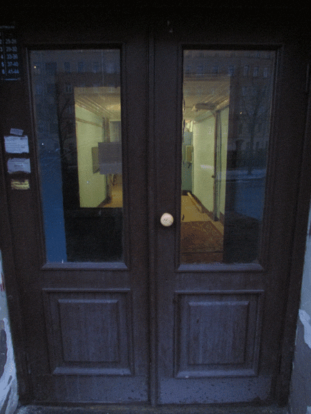Показана деревянная двустворчатая дверь со стеклом, установленная в подъезде дома, в старом фонде. 