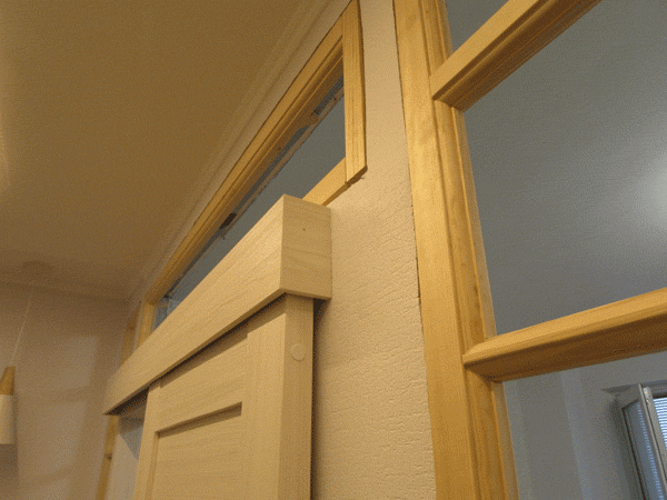 Откатная дверь выступает из перегородки, механизм скрыт декоративной накладкой. Шумоизоляция не очень у откатных дверей, но удобно.
