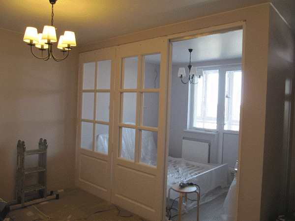 Деревянная перегородка со стеклом сделана с откатной дверью. Она зонирует помещение, остекая спальное место. 