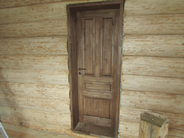 Деревянная дверь установлена в бревенчатом доме, срубе