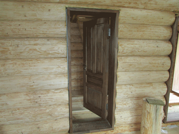 Классическое исполнение, массивная деревянная дверь в загородном деревенском доме, который сделан из окорёного бревна.