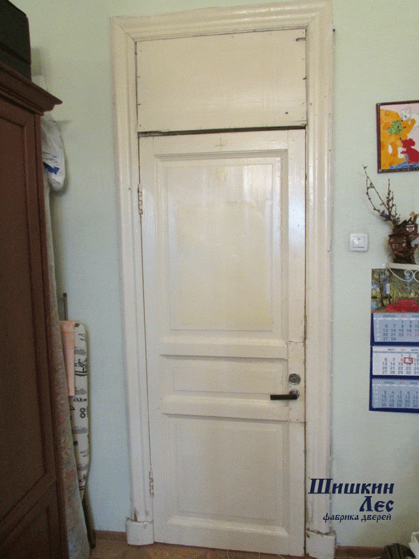 Старая дверь белого цвета с потрёпанным временем видом требует замены на новую. С фрамугой.